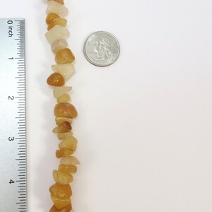 May include: A strand of light brown and white gemstone beads, approximately 4 inches long, next to a US quarter for size comparison.