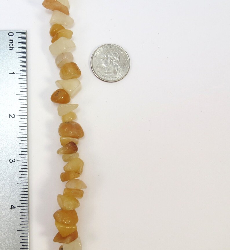 May include: A strand of light brown and white gemstone beads, approximately 4 inches long, next to a US quarter for size comparison.