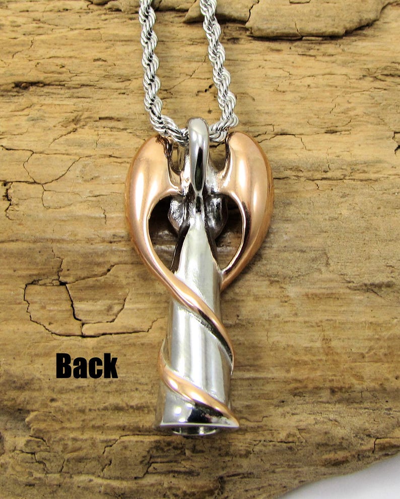 K&ouml;nnte beinhalten: Ein silberner und ros&eacute;goldener Engel-Anh&auml;nger mit einem gedrehten Design, der an einer silbernen Seilkette h&auml;ngt. Der Engel hat ausgebreitete Fl&uuml;gel und das Wort "Back" ist auf dem Holzgrund aufgedruckt.