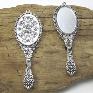 May include: Two silver-toned ornate hand mirrors with oval-shaped reflective surfaces. The mirrors have intricate floral and scroll designs on the frames and handles.