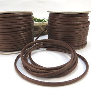 May include: Two spools of brown waxed cotton cord, with one spool unwound and lying on a white surface.