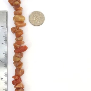 May include: A strand of orange and yellow gemstone beads, approximately 4 inches long, next to a US quarter for size comparison.
