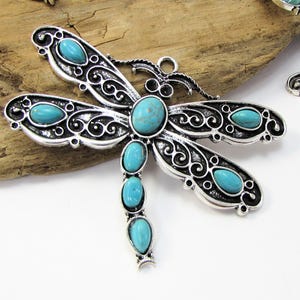 May include: Silver dragonfly pendant with turquoise blue stones. The dragonfly has intricate details and a loop for hanging.
