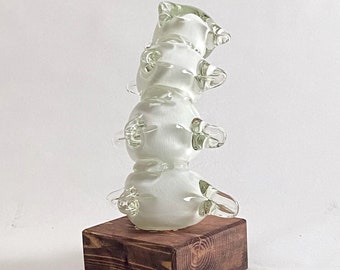 May include: A white glass sculpture with a stacked, organic shape, resembling a spine. The sculpture is mounted on a dark brown wooden base.