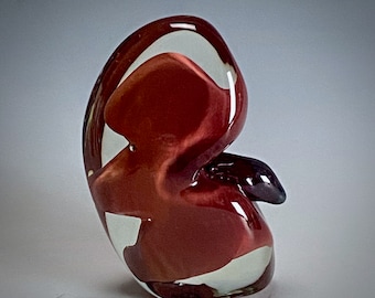 May include: A red and white glass sculpture with an abstract shape. The sculpture is made of clear glass with red and white swirls.