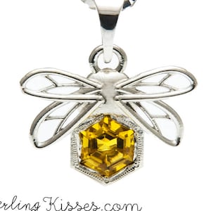 May include: A silver bee pendant necklace with a yellow hexagonal gemstone. The bee has delicate wings and a detailed body.