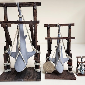 Pu&ograve; includere: Tre espositori per squali in legno, ognuno con uno squalo grigio appeso a delle corde. Il display pi&ugrave; grande ha la scritta "JAWS" stampata sul lato.