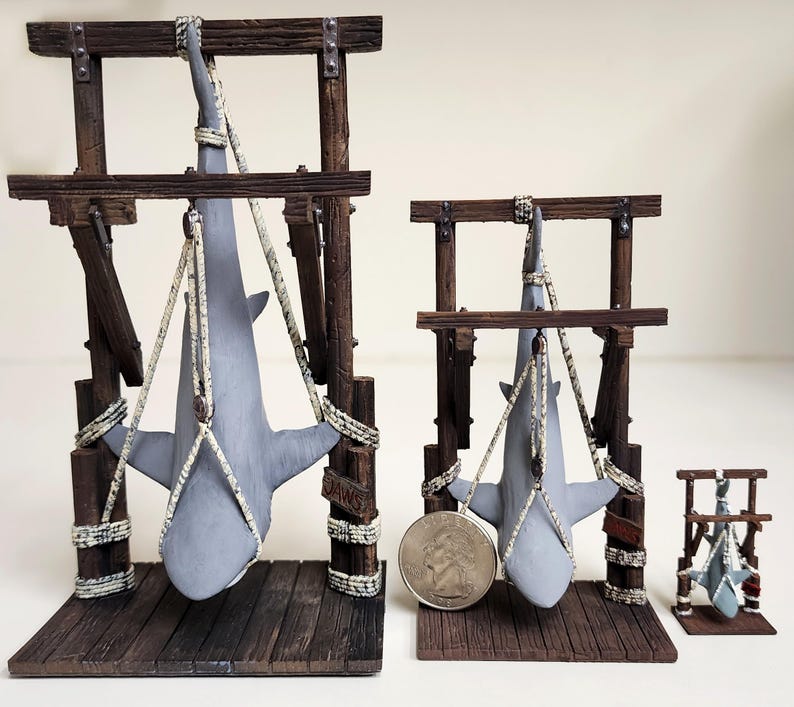 Pu&ograve; includere: Tre espositori per squali in legno, ognuno con uno squalo grigio appeso a delle corde. Il display pi&ugrave; grande ha la scritta "JAWS" stampata sul lato.