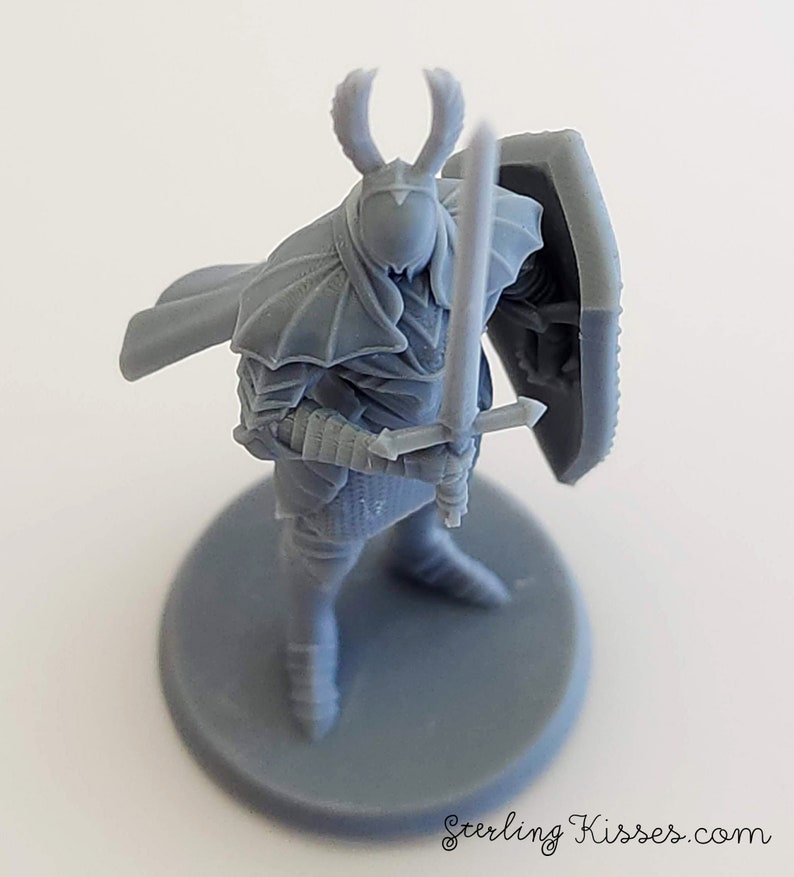 May include: Gray plastic miniature figurine of a knight wearing armor and holding a sword and shield. The knight is standing on a round base.