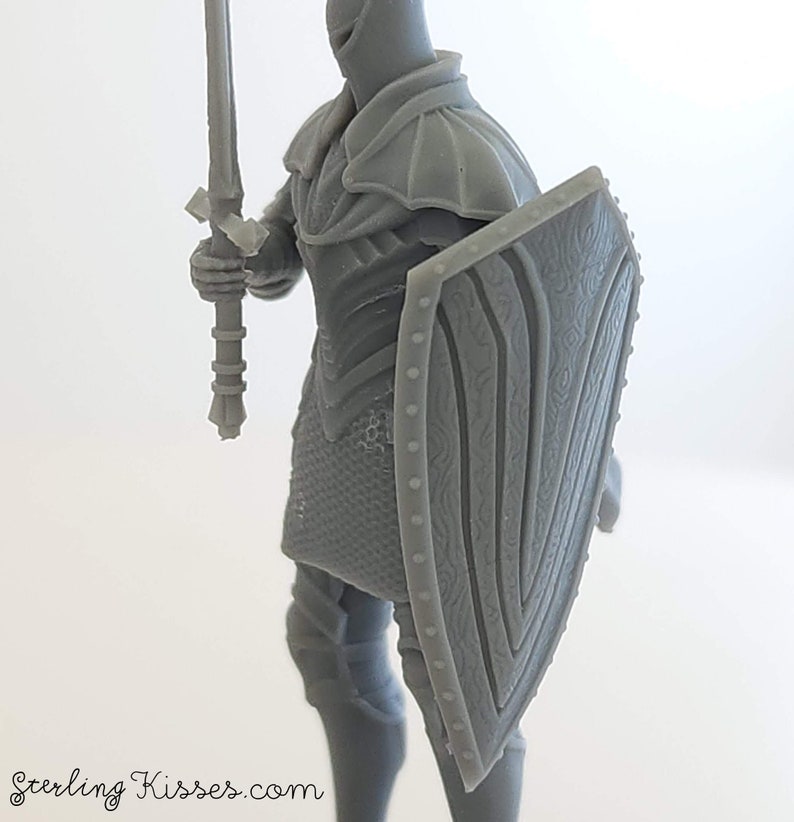 May include: A gray plastic miniature of a knight wearing armor and holding a sword and shield. The shield has a detailed design.