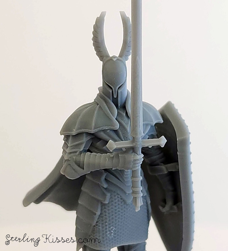 May include: A gray plastic miniature figurine of a knight wearing armor and holding a sword and shield. The knight has a winged helmet.