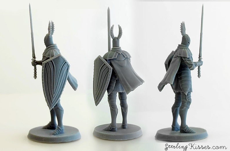 May include: A gray plastic miniature figurine of a knight wearing armor and a cape, holding a sword and shield. The knight has a horned helmet with wings on the side.