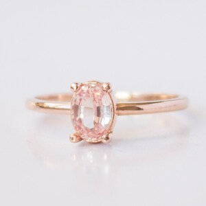 May include: A delicate rose gold ring with a pale pink oval gemstone.