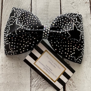 Puede incluir: Un gran lazo negro con pedrería, decorado con una tarjeta a rayas blancas y negras que dice "BowChik by Jenny Shaw CHEER Bows & More. Owner/Designer www.facebook.com/BowChikbyJennyShaw/ETSY jtzgir07@aol.com"