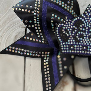 Puede incluir: Un lazo de animadora negro y morado con pedrer&iacute;a. El lazo tiene un dise&ntilde;o de estrella con rayas moradas.