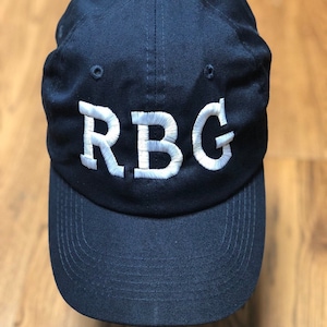 May include: A navy blue baseball cap with a white embroidered "RBG" on the front.