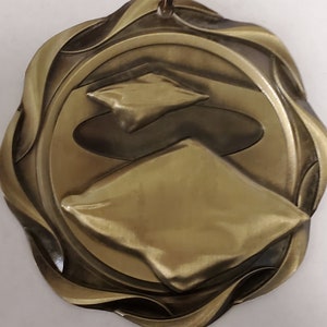 May include: A gold-colored medal with a wavy, ornate border. The center of the medal features two overlapping, stylized diamond shapes.
