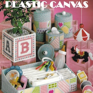Może przedstawiać: Broszura z wzorami rękodzielniczymi Leisure Arts zatytułowana Projects for Baby in Plastic Canvas, prezentująca różne ręcznie wykonane przedmioty, w tym kwadratową osłonkę na doniczkę, pojemniki z pokrywkami, prostokątny organizer oraz karuzelę z konikiem.
