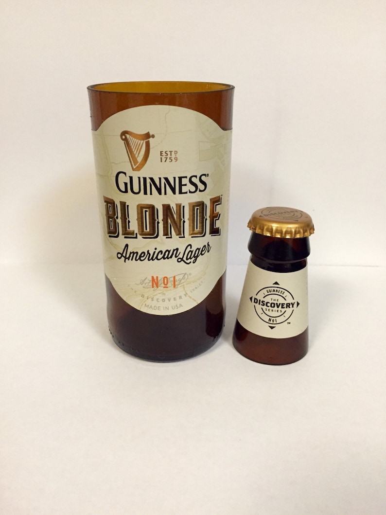 Może przedstawiać: Dwie szklane butelki, jedna większa od drugiej. Większa butelka jest brązowa i ma etykietę z napisem "Guinness Blonde American Lager No.1 Discovery Series Made in USA". Mniejsza butelka jest brązowa i ma etykietę z napisem "Guinness The Discovery Series No.1".