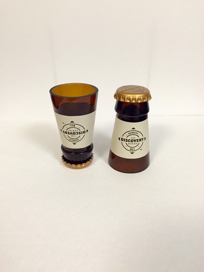 Puede incluir: Dos vasos de chupito de vidrio marr&oacute;n con tapas doradas. Los vasos est&aacute;n etiquetados con "The Discovery Series" y "No. 1".