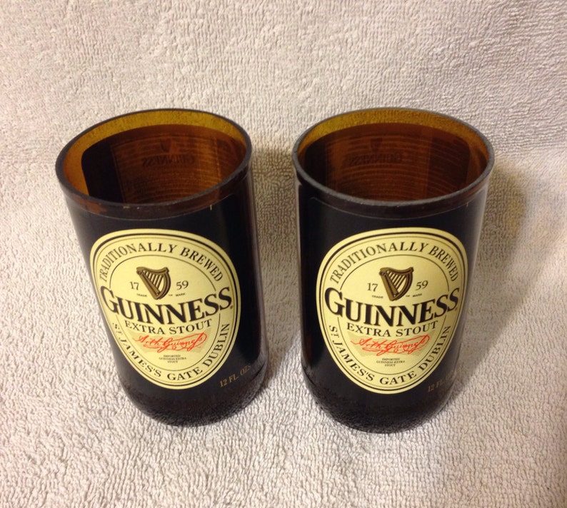 May include: Two black glass mugs with a brown top, each with a Guinness label that reads "Traditionally Brewed 17 59 Guinness Extra Stout St. James's Gate Dublin 12 fl oz."