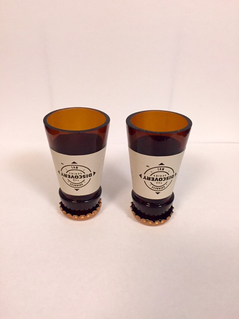 Puede incluir: Dos vasos de chupito de vidrio marr&oacute;n con tapas de botella doradas. Los vasos est&aacute;n decorados con una etiqueta blanca que dice "The Discovery Series No. 1".