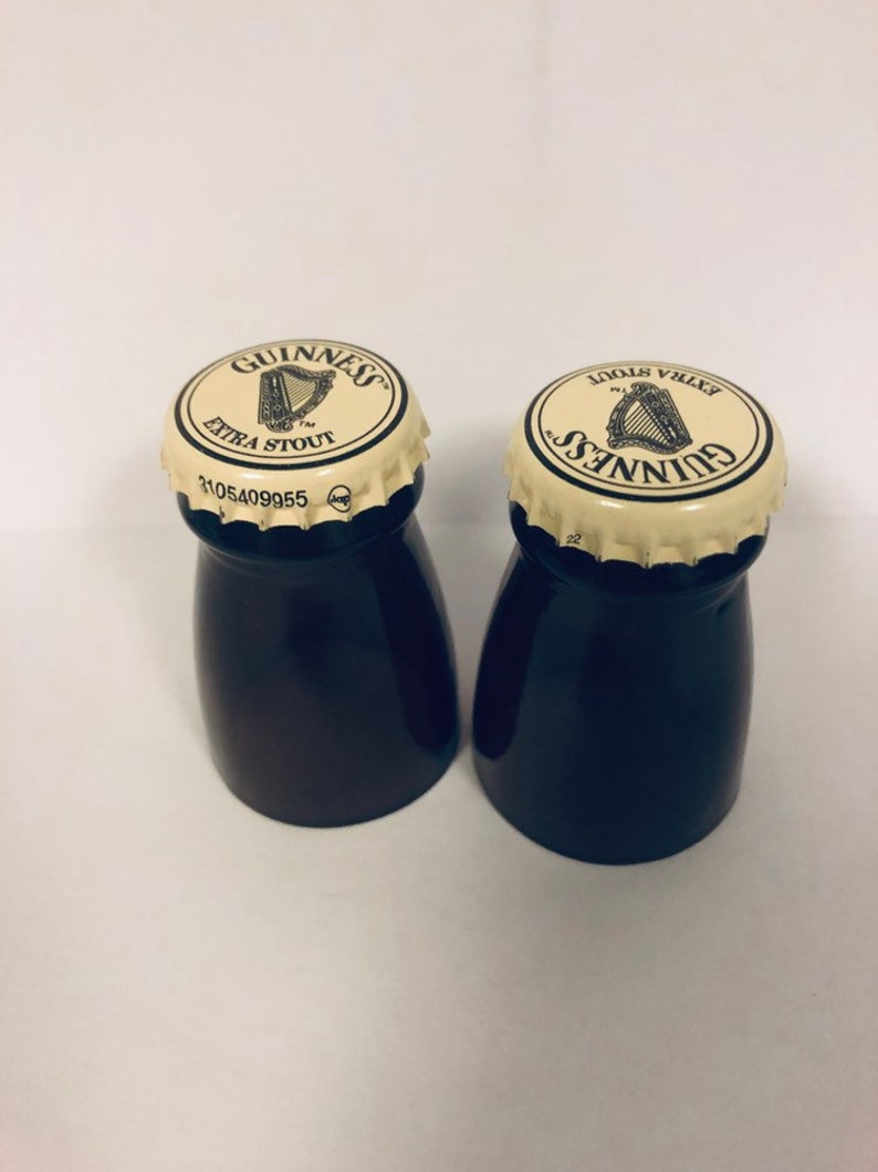 May include: Two black glass salt and pepper shakers with white lids. The lids have the Guinness logo and text "Extra Stout" printed on them.