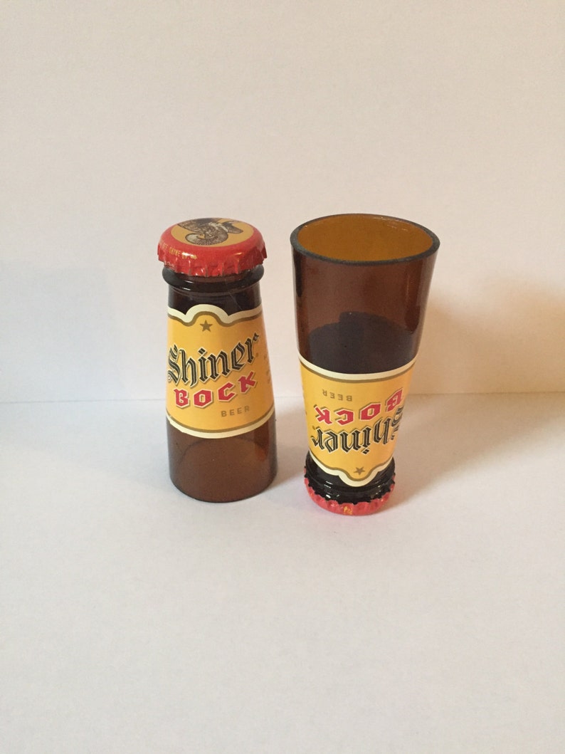 Pode incluir: Duas garrafas de vidro em miniatura, uma cheia de um l&iacute;quido castanho e etiquetada "Shiner Bock Beer", a outra vazia e etiquetada "Shiner Bock Beer".