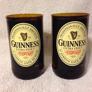 May include: Two brown glass beer bottles with black labels. The labels feature the Guinness logo, the text "Traditionally Brewed", "Guinness Extra Stout", "St. James's Gate Dublin", and "12 fl oz".