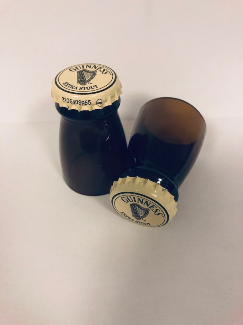 May include: Two small brown glass bottles with white caps. The caps have the Guinness logo and the words "Extra Stout" printed on them. One bottle is lying on its side and the other is standing upright.