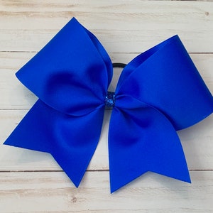 May include: A large royal blue cheer bow with a glitter center. The bow is tied with a black elastic.