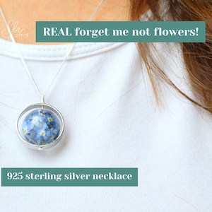 May include: A silver necklace with a round pendant featuring real forget-me-not flowers encased in resin. The pendant is suspended from a delicate silver chain. The necklace is labelled "925 sterling silver necklace" and "REAL forget me not flowers!"