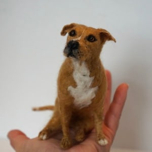 May include: A brown and white needle felted dog figurine. The dog is sitting with its head tilted up and its ears perked. The figurine is about the size of a person's hand.