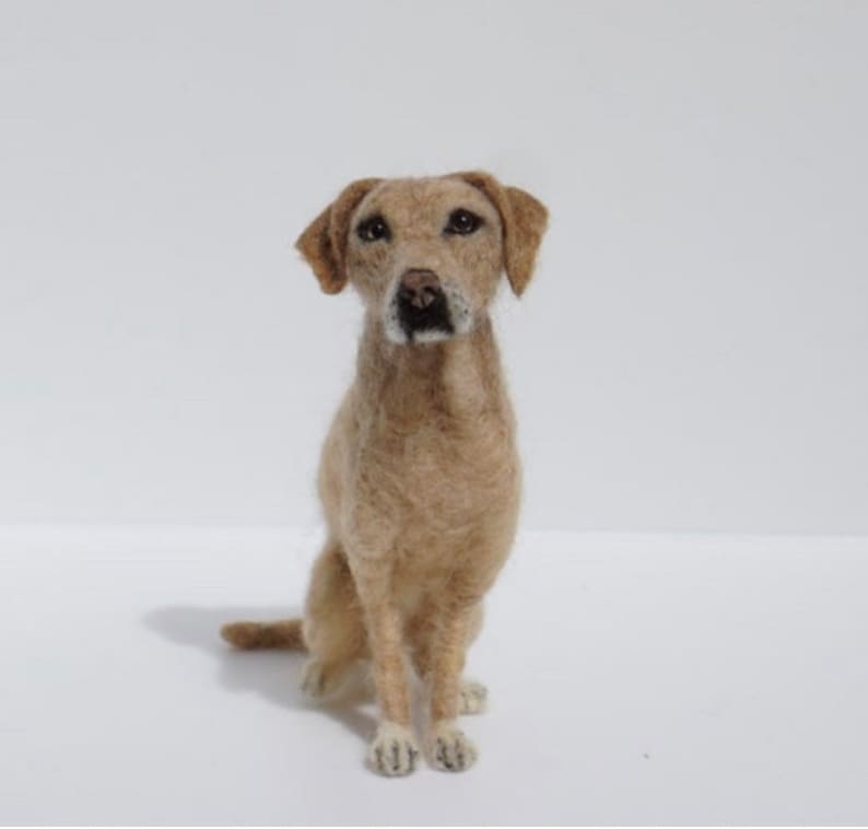 May include: A needle felted dog sculpture, a realistic depiction of a Labrador Retriever, sitting with its paws crossed and looking directly at the camera.