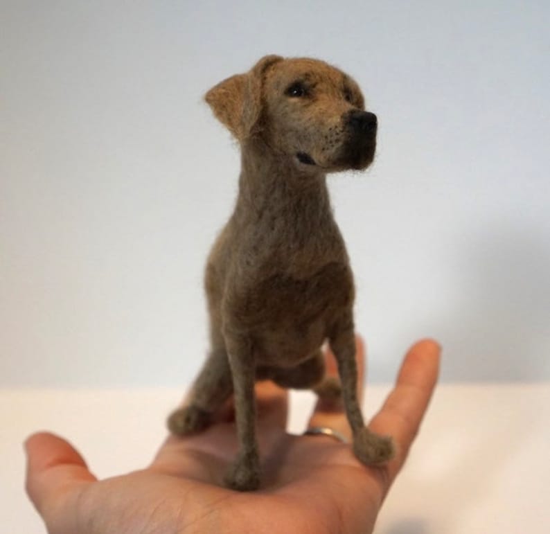 May include: A brown needle felted dog figurine. The dog is sitting with its head tilted to the side and its ears perked up. The figurine is detailed with realistic fur and features.