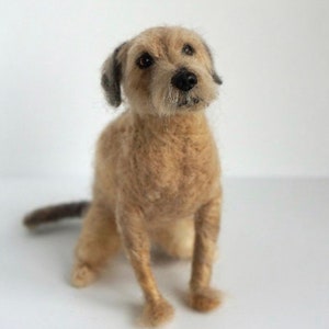 May include: A needle felted dog sculpture, sitting with its front paws forward and its tail curled behind it. The dog is brown and white with a black nose and black eyes.