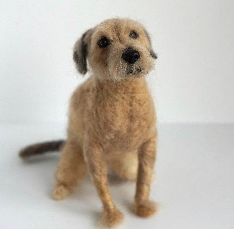 May include: A needle felted dog sculpture, sitting with its front paws forward and its tail curled behind it. The dog is brown and white with a black nose and black eyes.