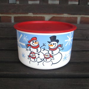 May include: A white and blue container with a red lid. The container features a snowman family design with snowflakes. The snowmen wear hats and scarves. A festive, seasonal storage container.