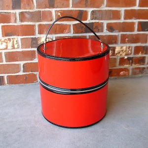 May include: A bright red, cylindrical handbag with a black zipper and trim. The bag has a black handle and a glossy finish. The bag is a vintage style and is likely made of a patent leather or similar material.