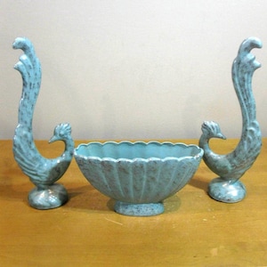 May include: A set of three ceramic decorative pieces. Two tall peacock figurines flank a scalloped-edge bowl. The pieces are a speckled turquoise color with a vintage aesthetic. The bowl is centered between the figurines.
