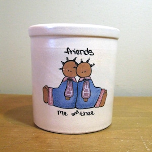 May include: A cream-colored ceramic kitchen utensil holder with a hand-painted design. The design features two figures in blue robes with the words "friends" and "me and thee".