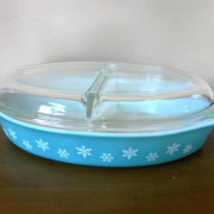 May include: A vintage turquoise divided casserole dish with a clear glass lid. The dish features a snowflake pattern around the rim. A classic piece of kitchenware.