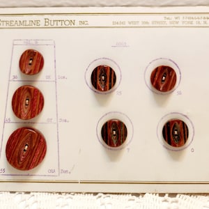 May include: A vintage display card from Streamline Button Inc. featuring various wooden buttons. The buttons have a reddish-brown wood grain pattern with a small hole for sewing. The card includes text and numbers.