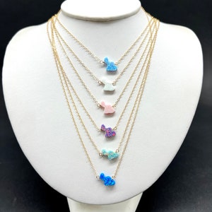 May include: A set of six gold necklaces with opal bunny pendants in various colors, including blue, light blue, white, pink, purple, and green. The necklaces are layered on a white mannequin bust.