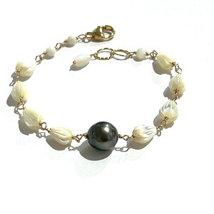 May include: A gold chain bracelet with white shell beads and a single black pearl in the center.
