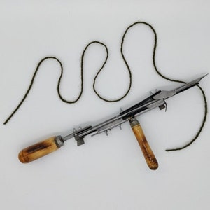 May include: A vintage wooden handled yarn winder with a metal mechanism and a green yarn attached.