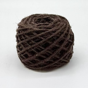 Peut inclure: Une pelote de fil brun foncé sur fond blanc. Le fil est étroitement enroulé, avec une texture visible et une forme légèrement irrégulière. Le fil semble être fait de fibres naturelles, adapté aux projets de tricot ou de crochet.