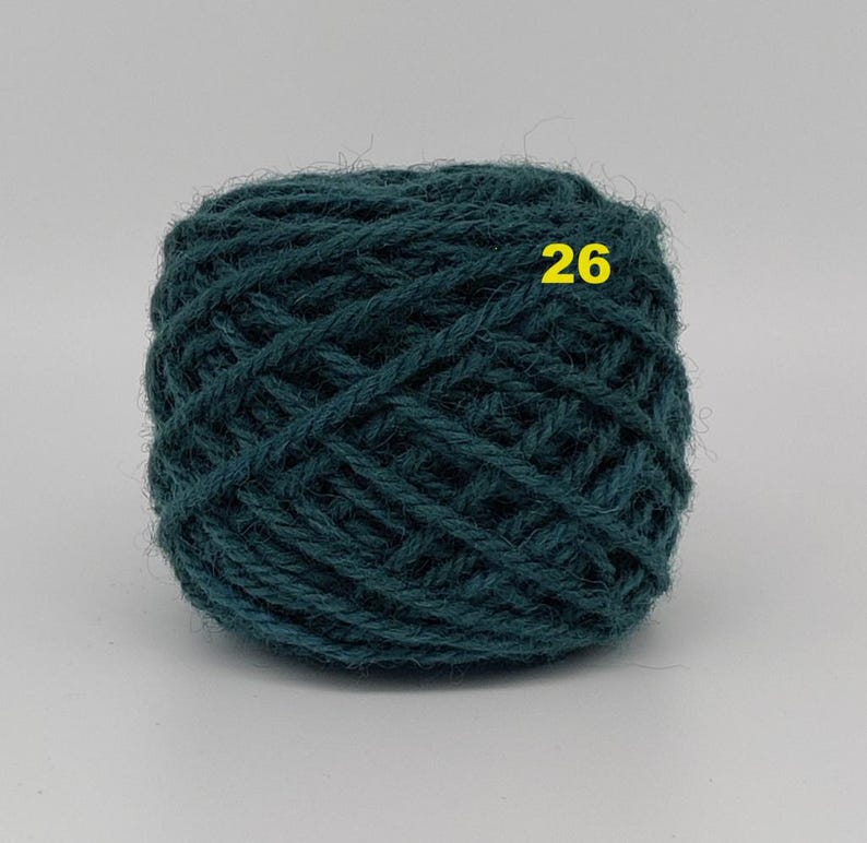 May include: A ball of teal-colored yarn with the number 26 in yellow. The yarn is tightly wound, showing the texture of the fibers. This yarn is suitable for knitting or crocheting projects.