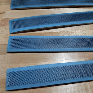May include: Four blue rubberized sanding belts with rows of metal bristles. The belts are arranged in a stack on a wooden surface.