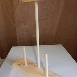 May include: Wooden yarn holder with three dowels and a top bar. The holder is made of natural wood and has a simple design.